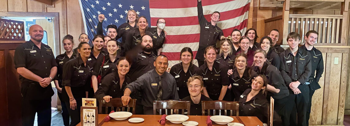 Cattlemens Staff gather in group photo in front of American Flag after serving Veterans 
